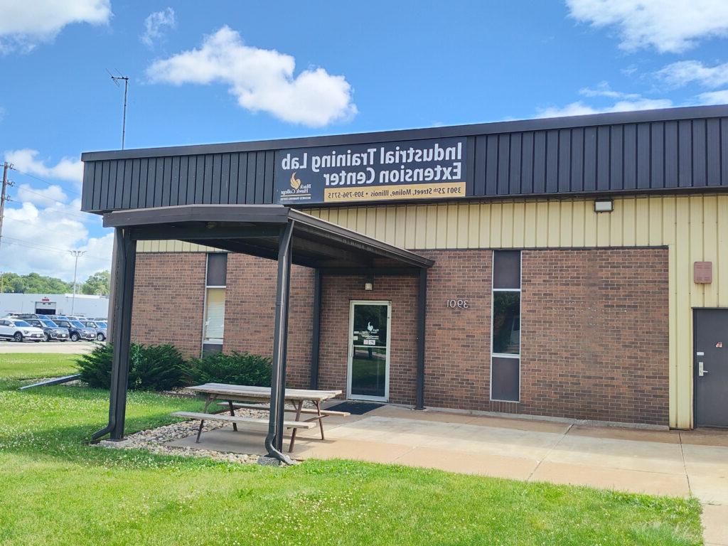 Black hawk college industrial training lab extension center. A brown brick building with black siding with a green lot in front of a blue sky.